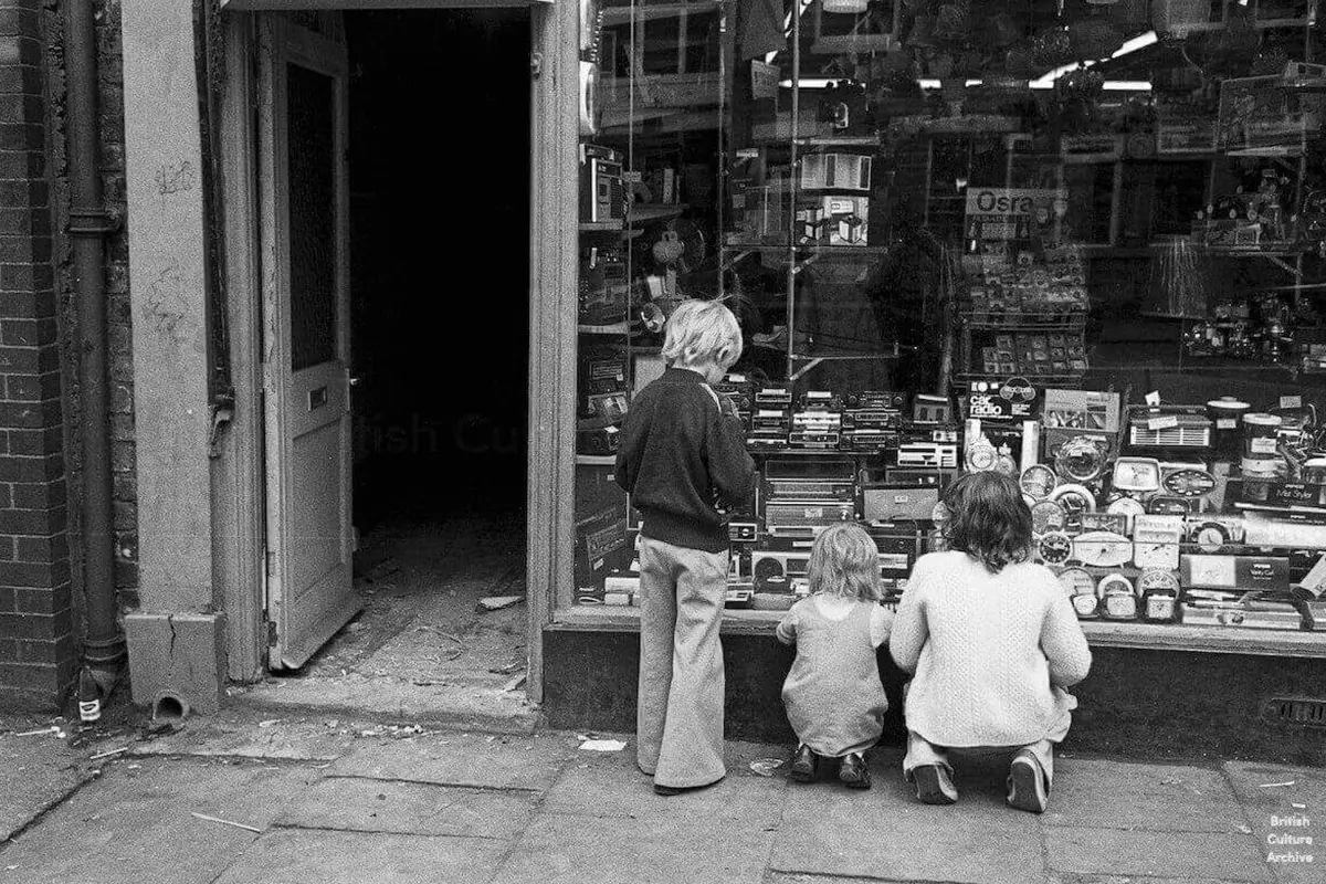 A photo by Luis Bustamante shows boys looking at radios through a shop window. Hull, 1970s.