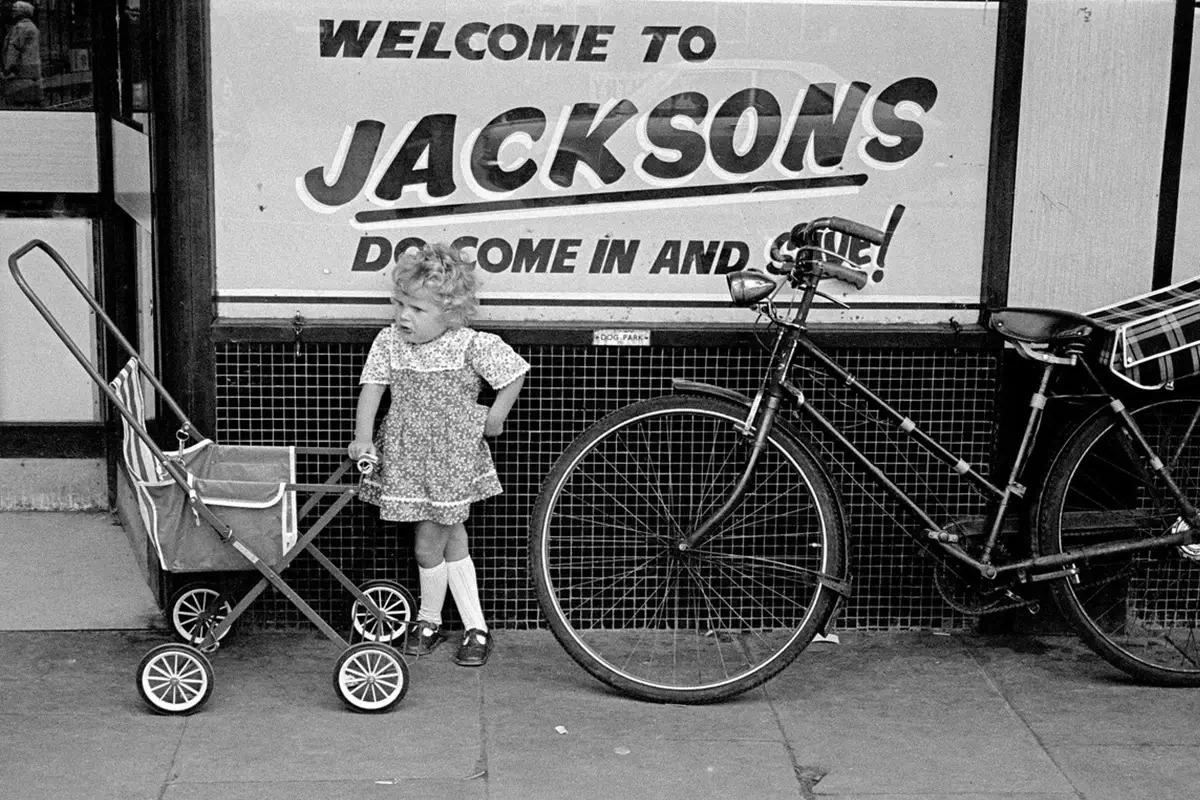 A photograph by Luis Bustamante shows a young girl outside Jacksons, Hull, in the 1970s.